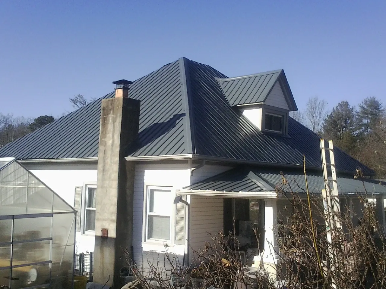 Dark blue standing seam metal roof on a white farmhouse with dormer — Slate & Tile Roof Repair by Roofing Brothers in Plainview