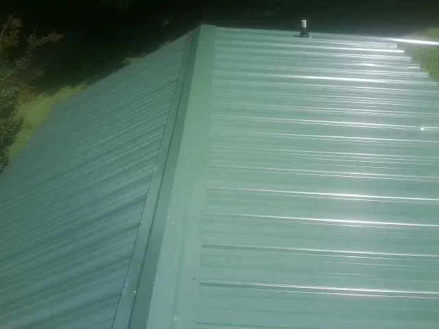 New green metal panels meeting at the ridge of a roof — Flat Roof Repair work by our crew in Plainview